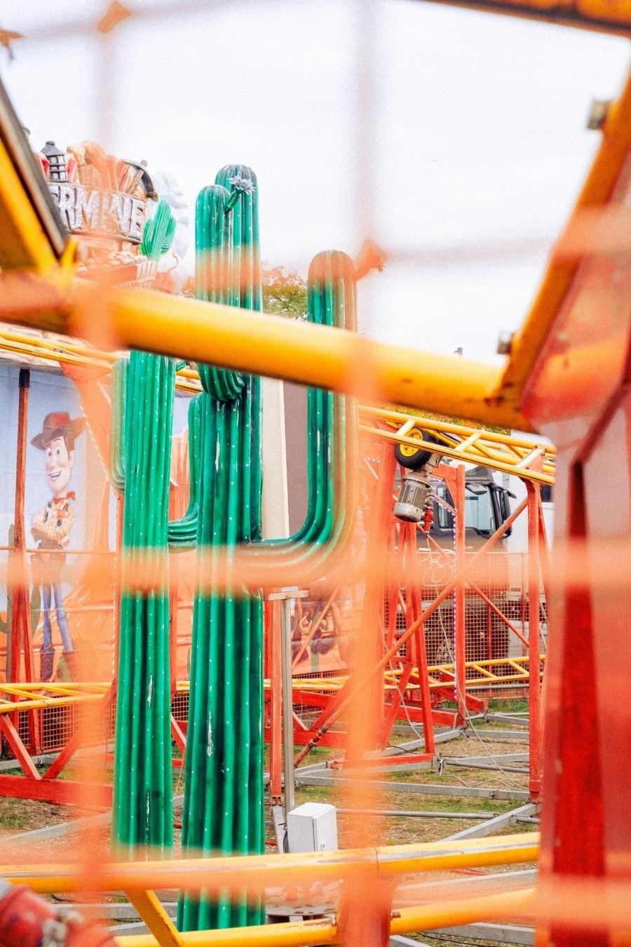 Foto durch orange Gitterstäbe einer Achterbahn. Schemenhaft ist ein Kaktus aus Plastik zu erkennen.