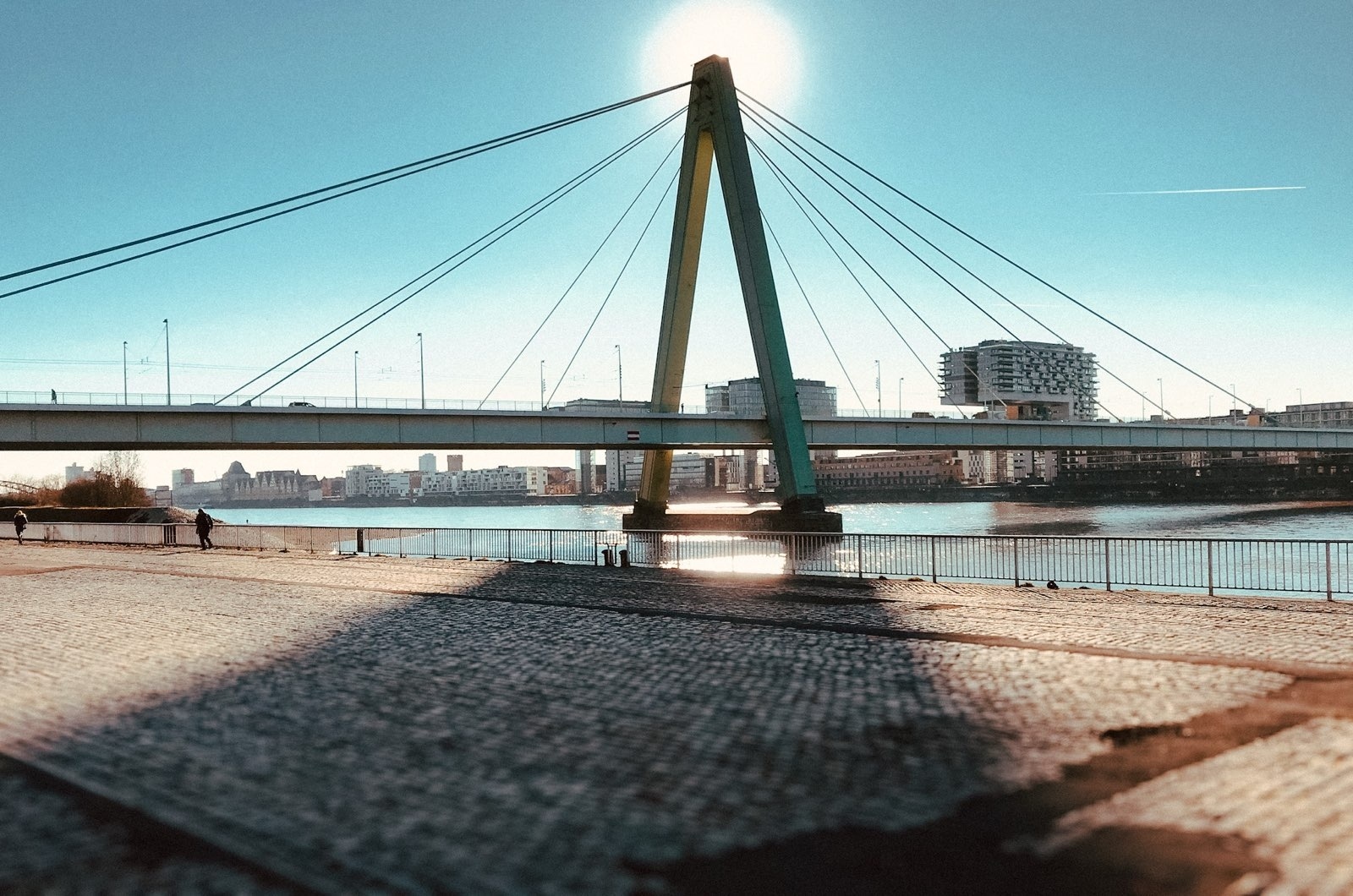 Severinsbrücke im Sonnenschein. Die Sonne steht direkt hinter einem BrückenPfeiler und wirft einen langen dreieckigen Schatten auf die Deutzer Werft.