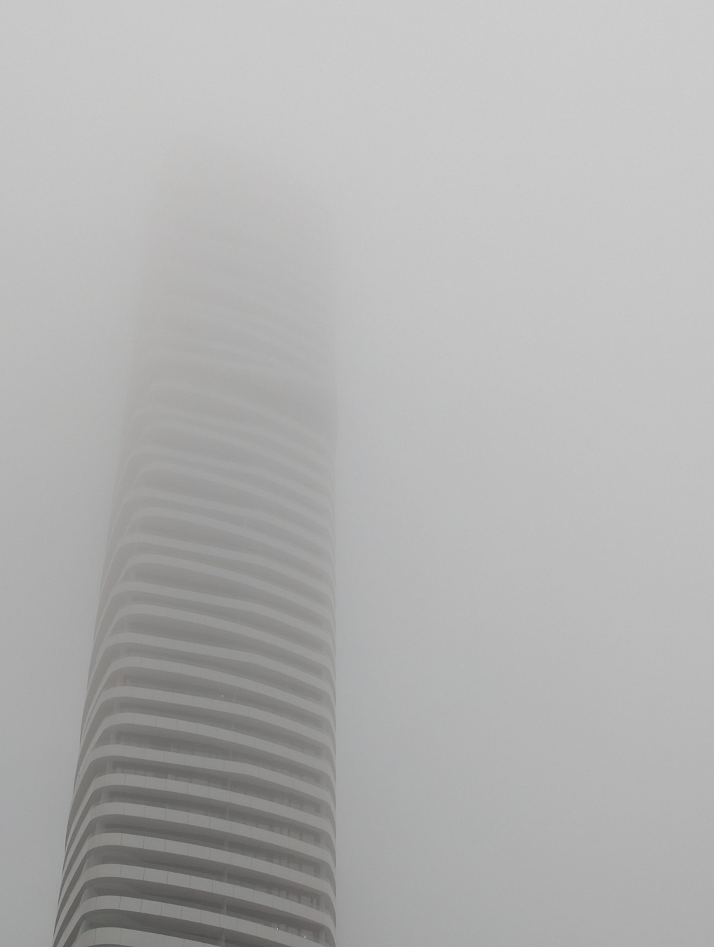 Foto eines weißen Hochhauses, das nach oben hin immer weiter im Nebel verschwindet, die Spitze ist nicht sichtbar, weil sie im dichten Nebel ist.