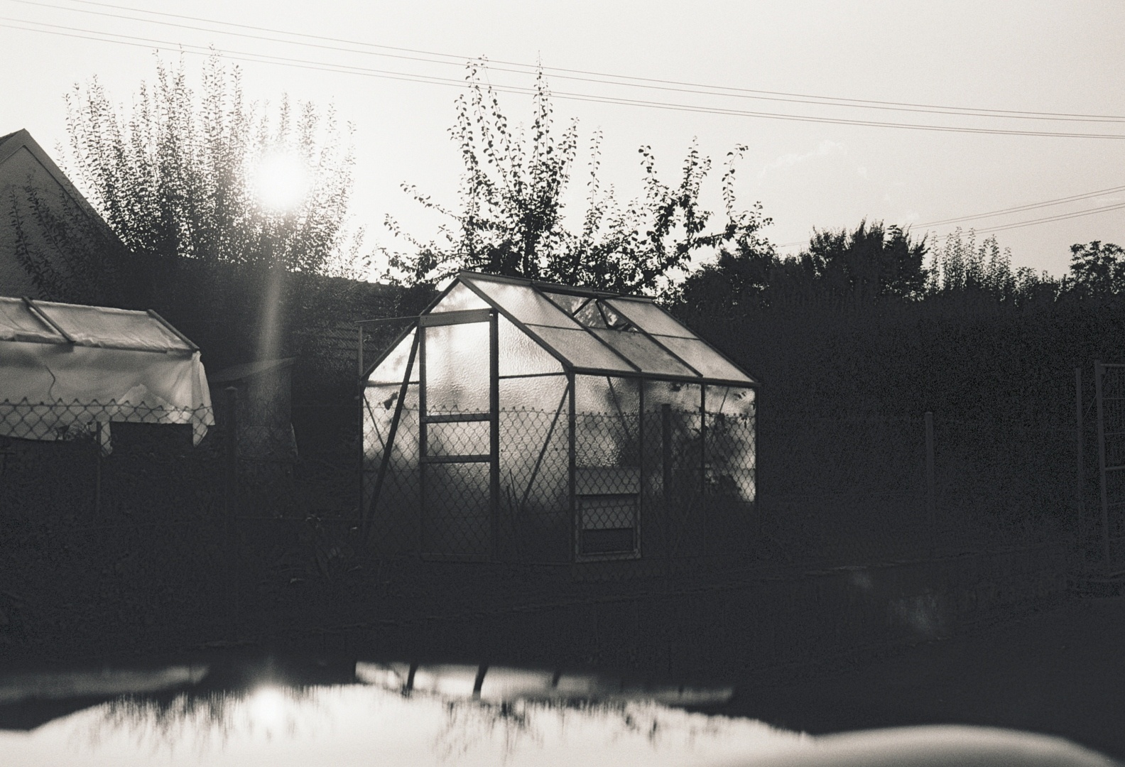 A black and white photo of a garden house that is reflected on a car roof.