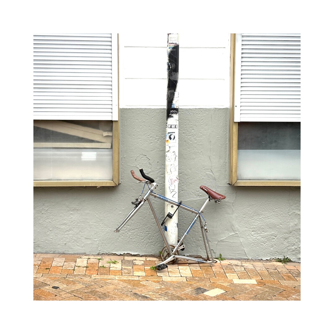 A bike frame locked to a street pole and stripped from it’s tires.