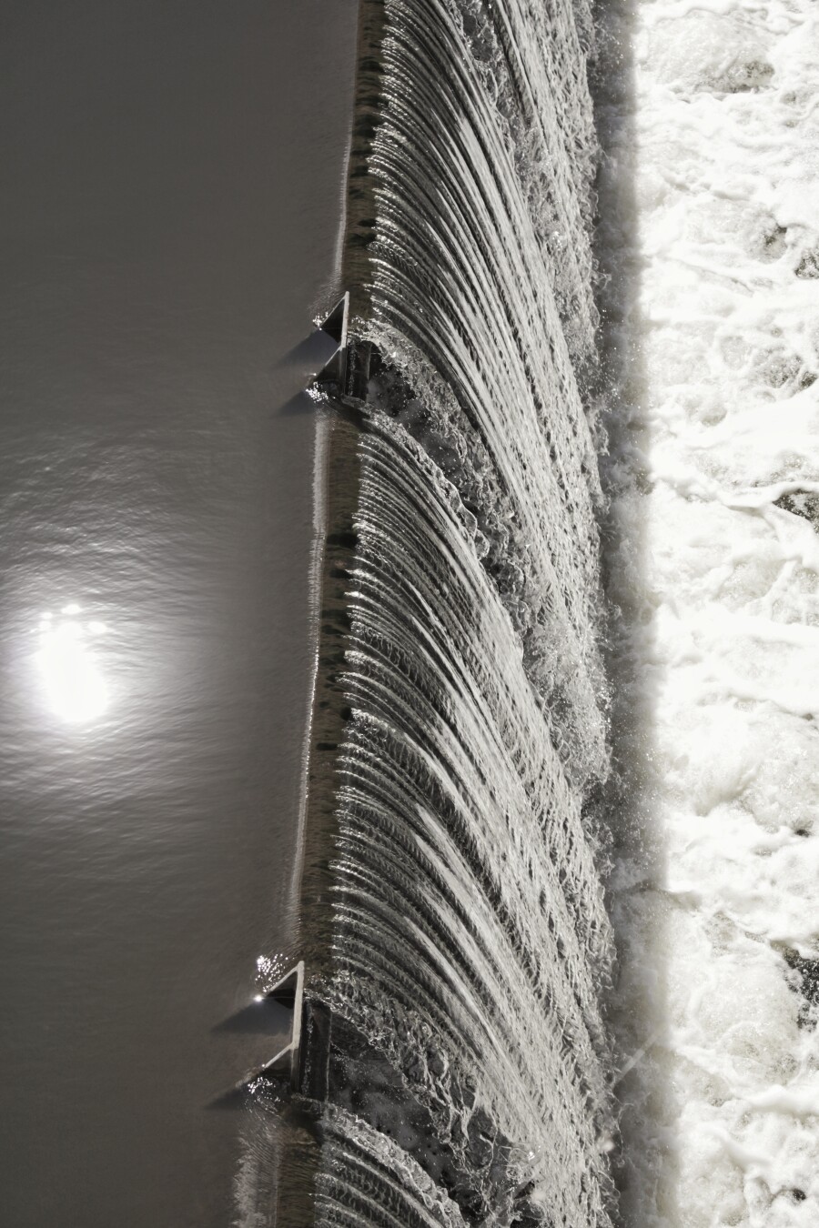 waterfall at the edge of a dam, the sun being reflected on the higher side
