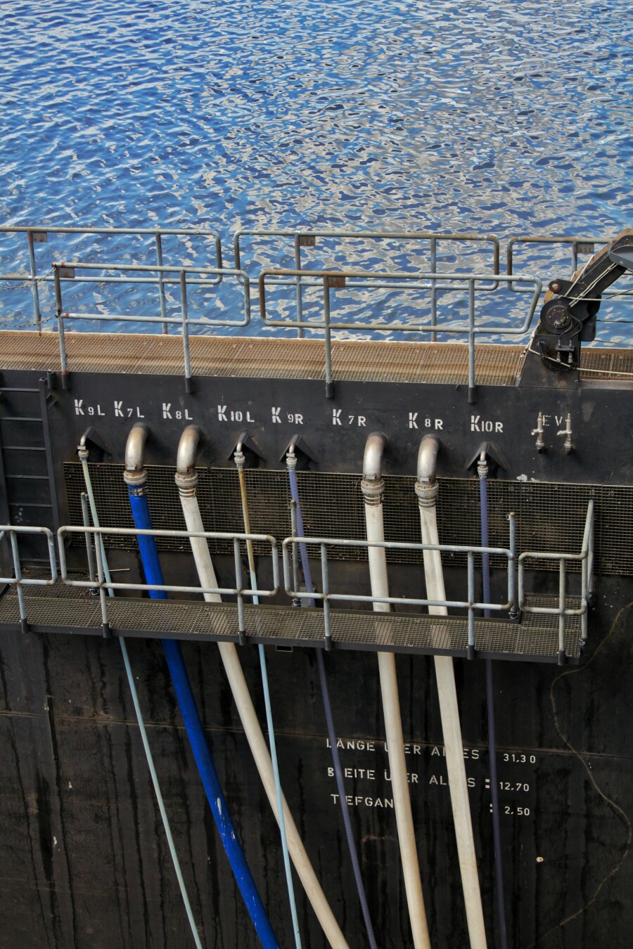 emptied section of a dam, with a wall holding back the water. there are multiple pipes going to the wall and off the edge of the picture. the connection points are labelled. on top of the wall, there's a small walkway.