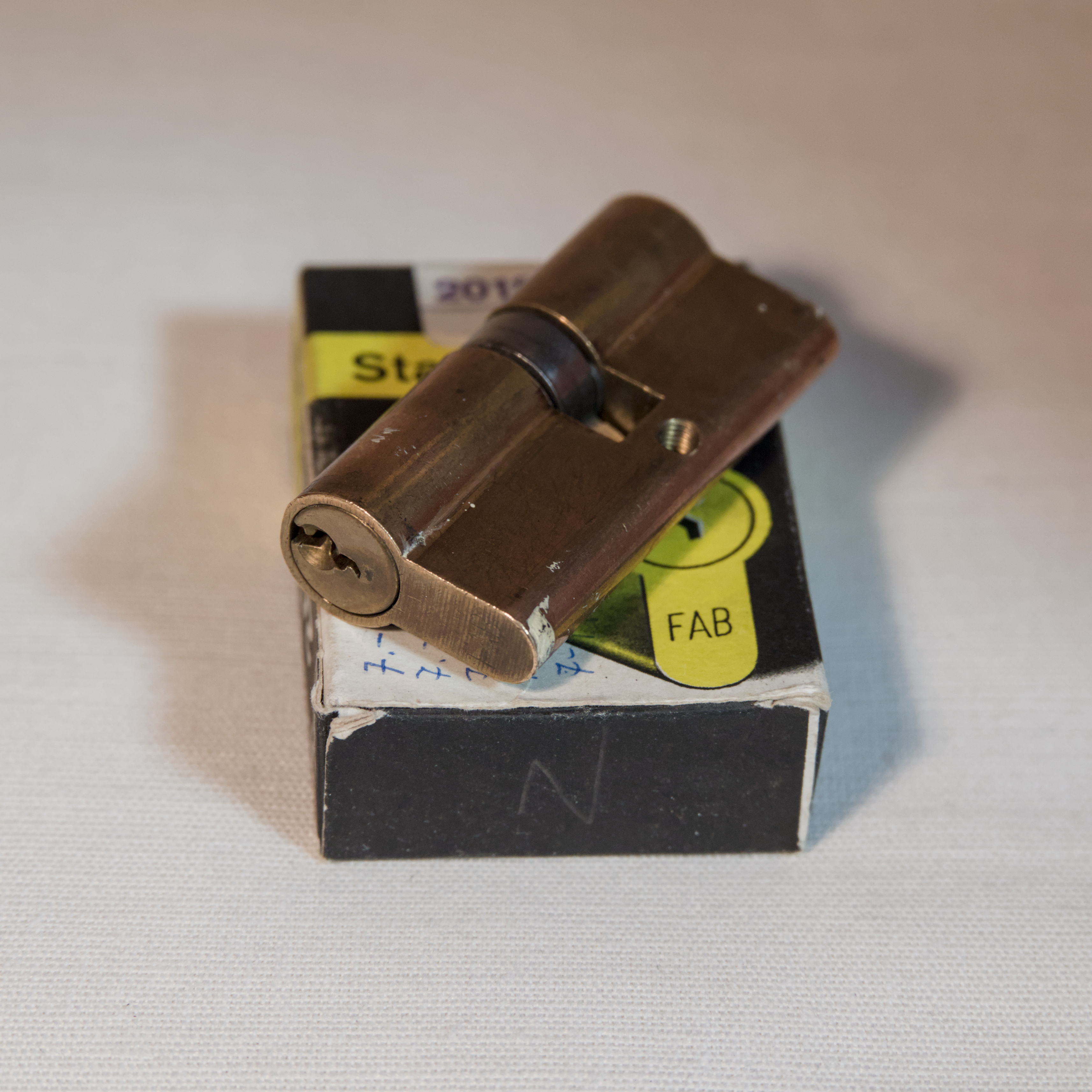A cylindrical lock, FAB 2018, resting on its box.