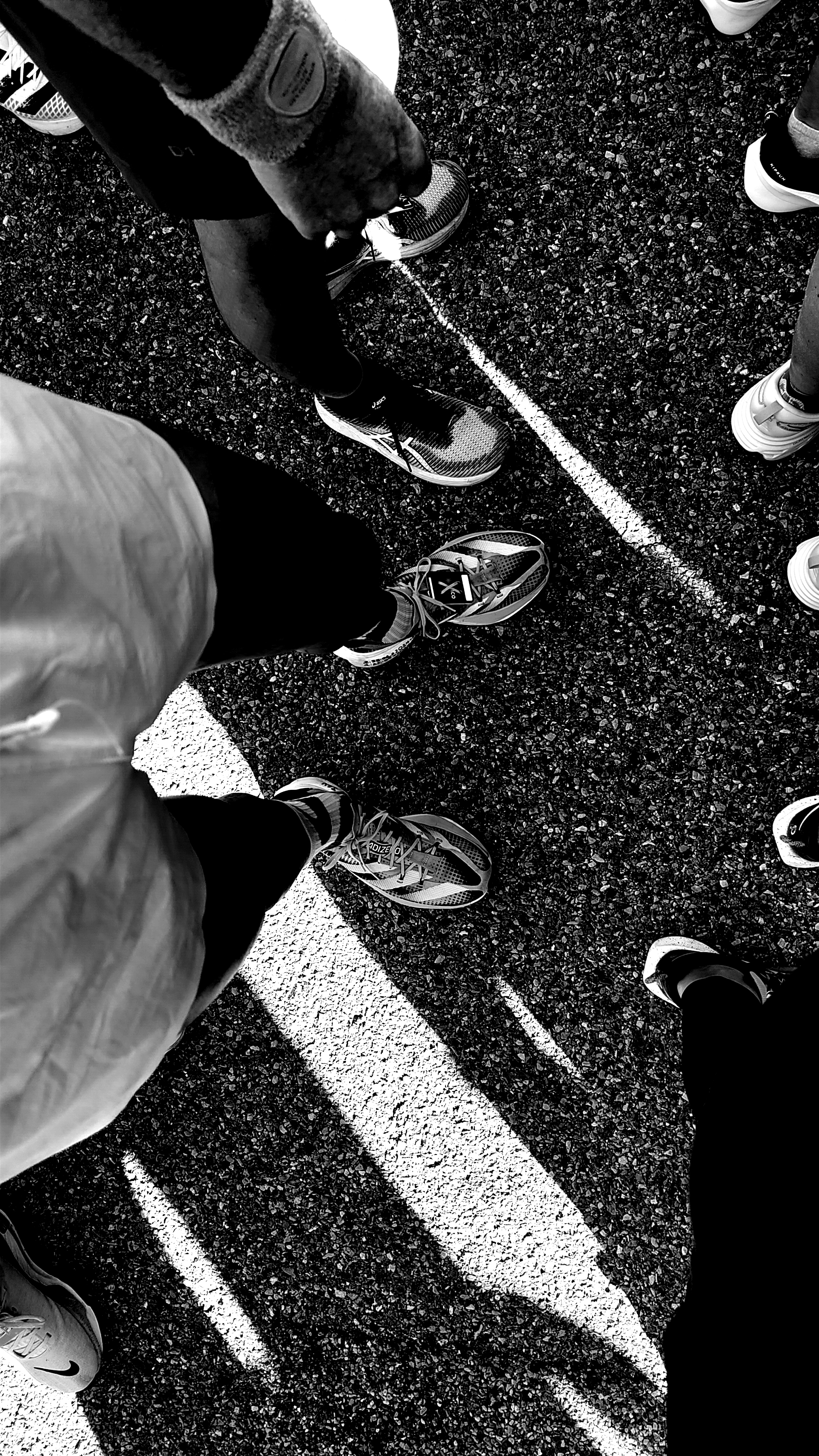 black and white picture of feet of runners seem from above over the asphalt with stark shadows