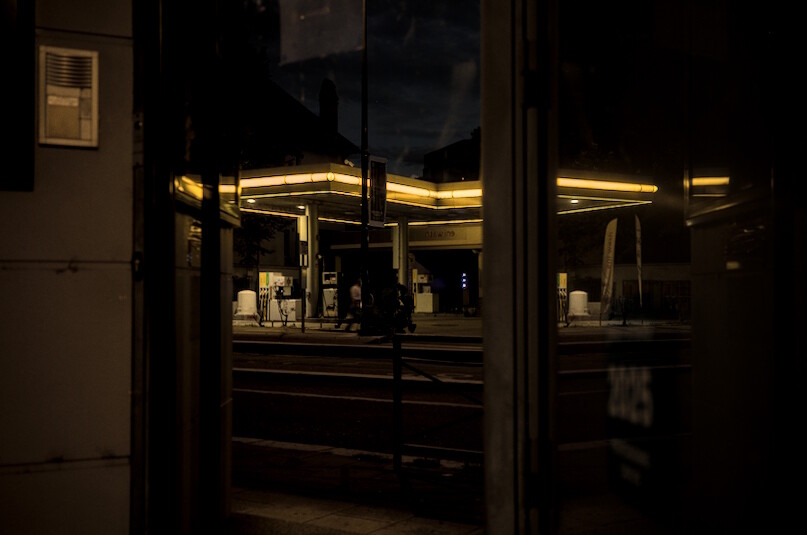 a yellow-lit gas station reflected in the window of a building at night